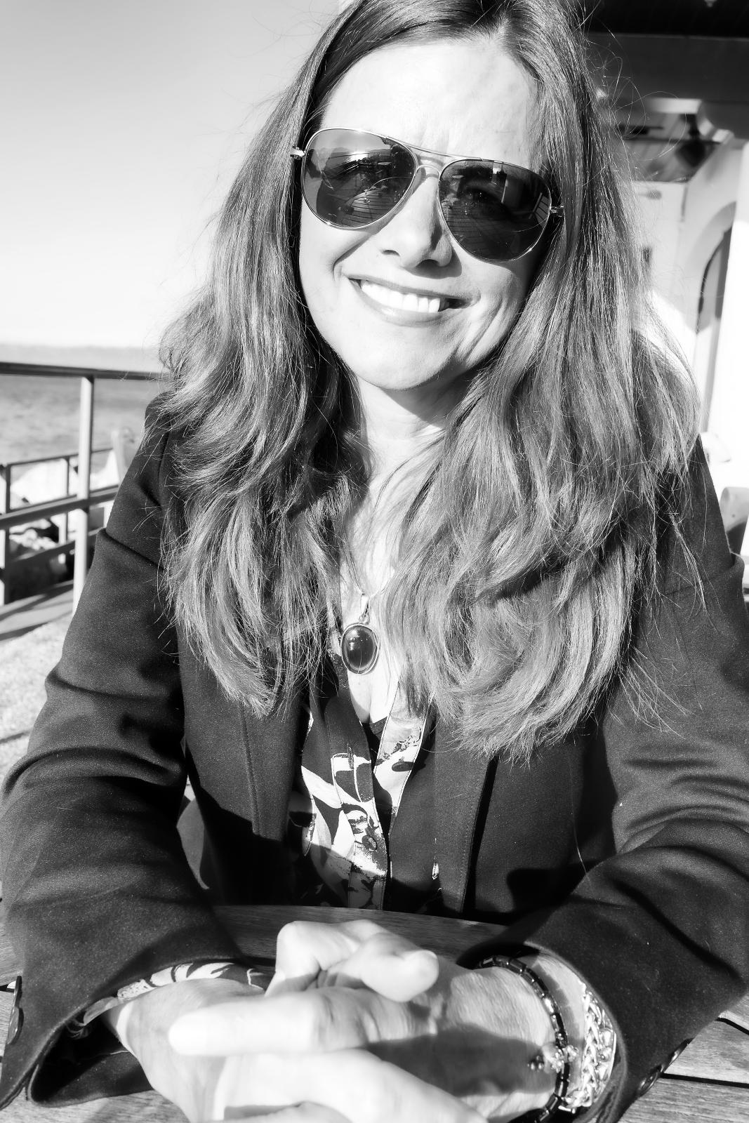 a smiling woman in sunglasses holds out her hand for the camera