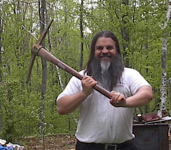 a bearded man holding a large axe in the woods