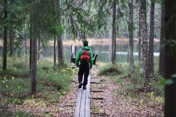 a man on a path with two backpacks walking in the woods