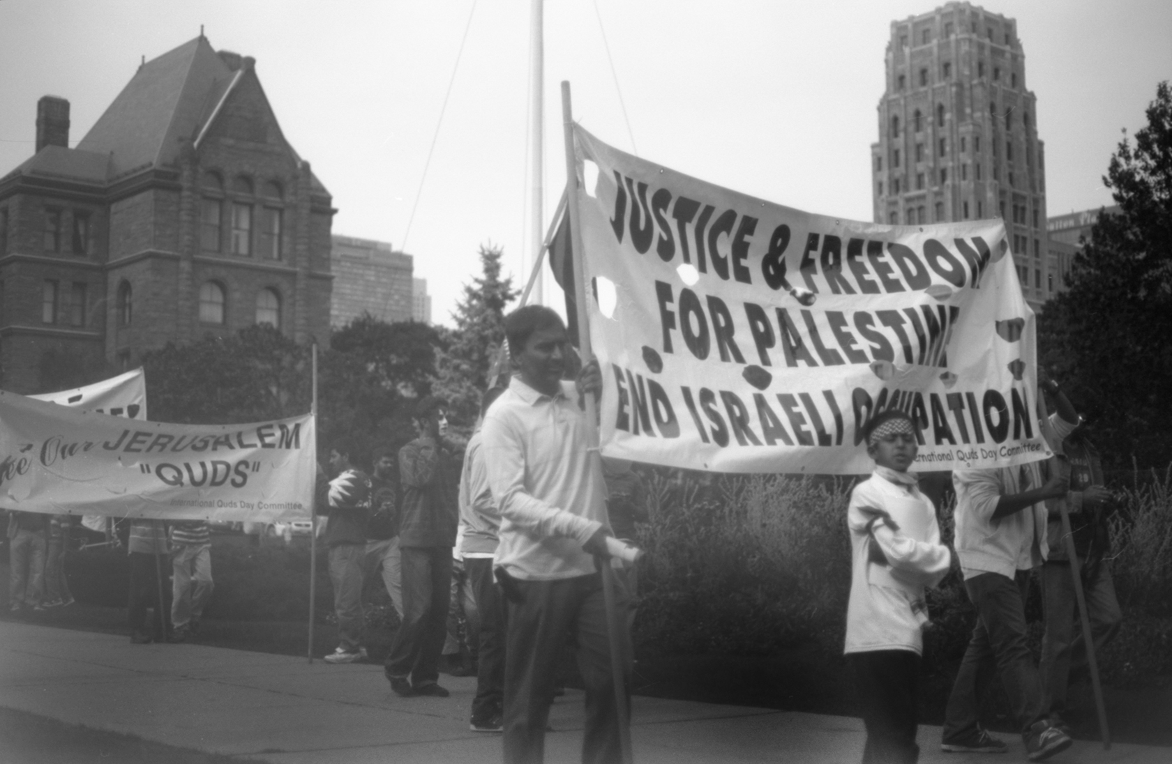 people standing on sidewalk with protest signs in the street