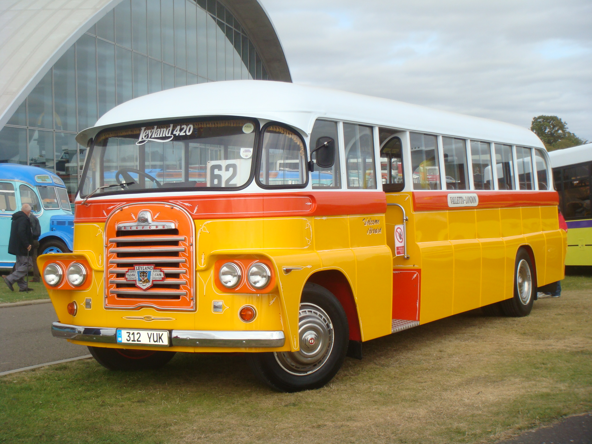 a yellow bus with red stripes parked next to other buses