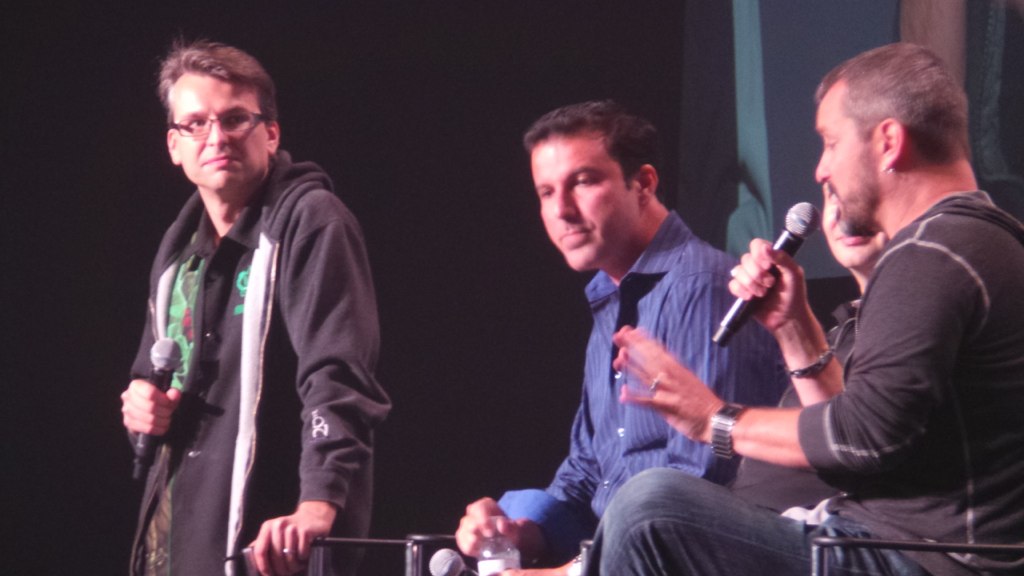three men standing on stage during a conversation