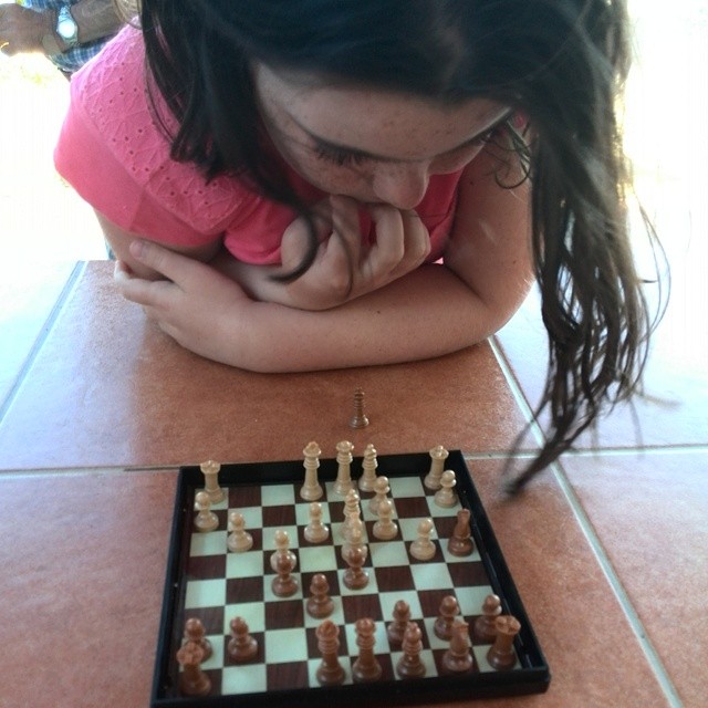 a girl leaning over to look at chess pieces