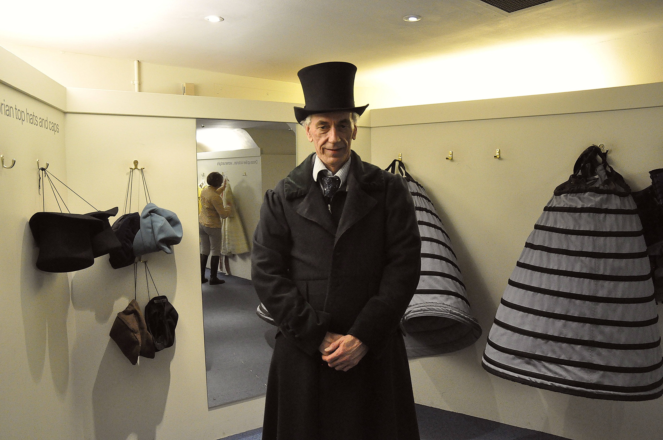 a man wearing a top hat and coat next to a wall