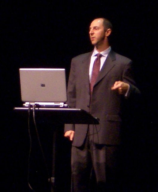 a man in suit standing near laptop on stage