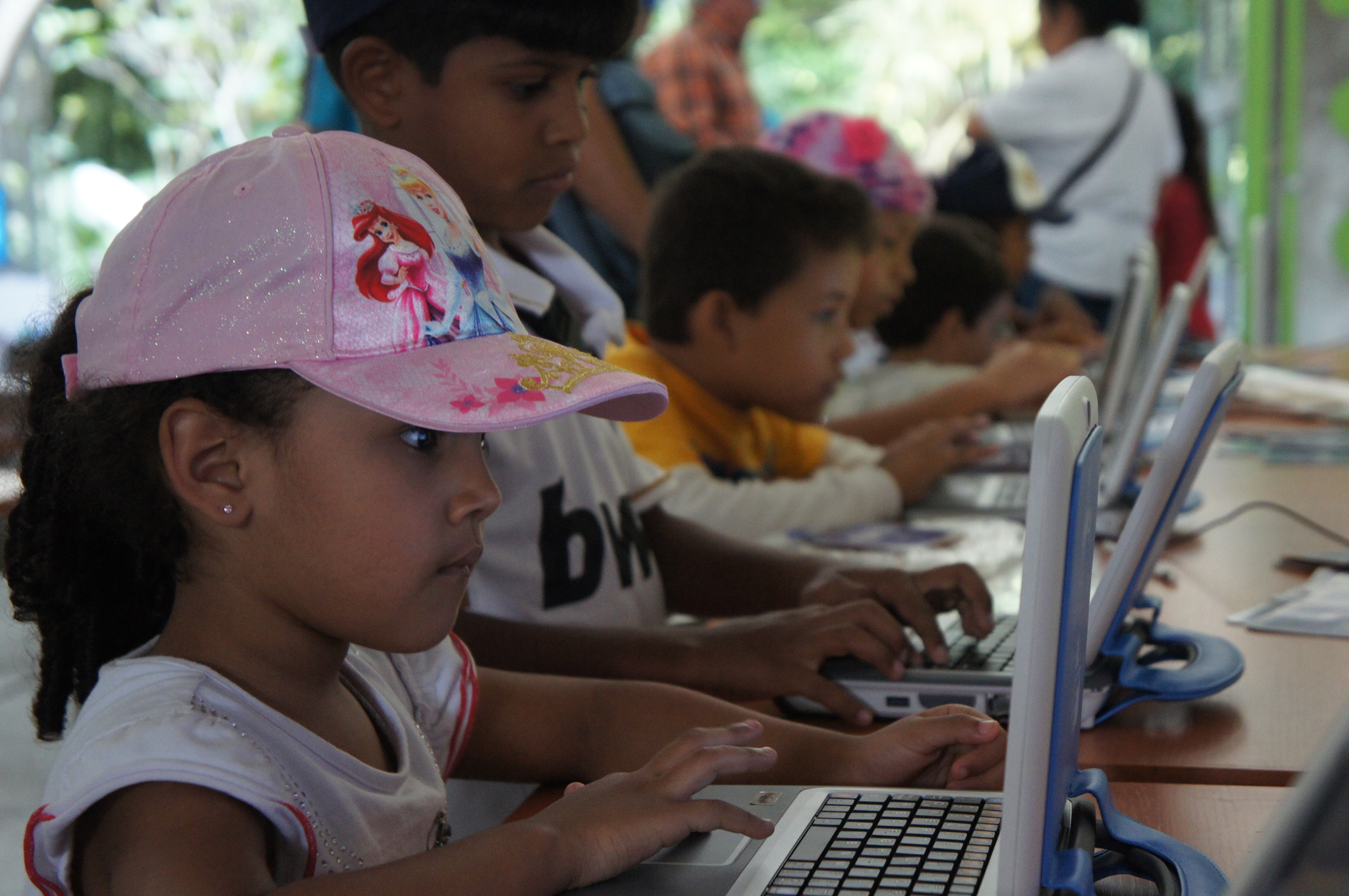 children using computers at a desk with others in the background