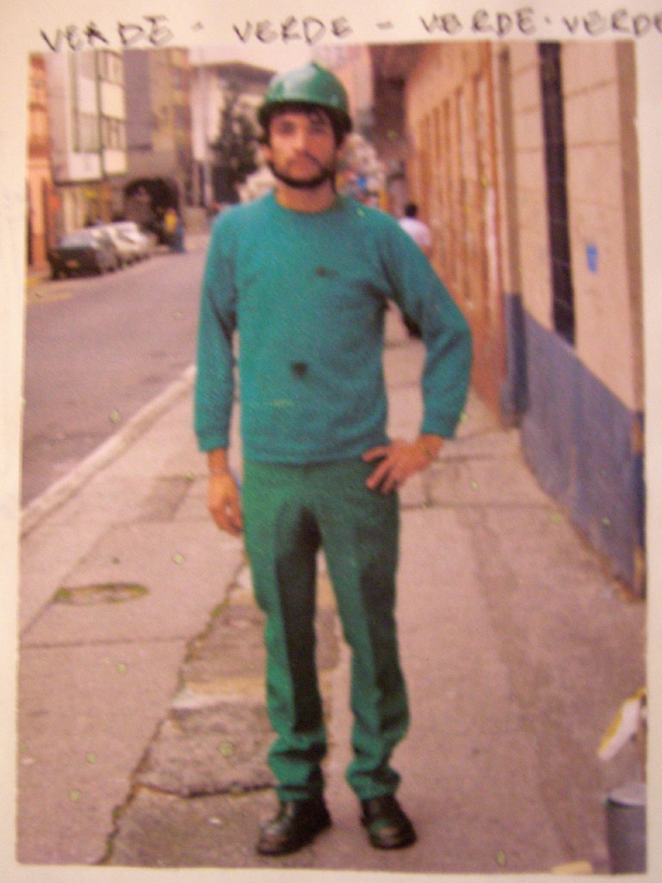 a man in green clothes is standing on a city sidewalk