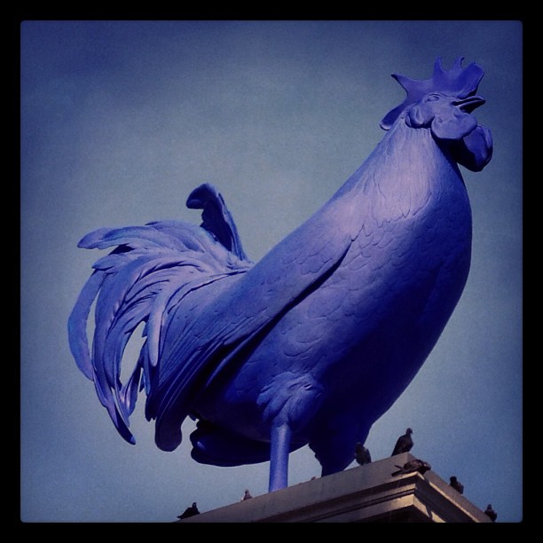 an odd looking statue of a blue rooster stands in front of a building