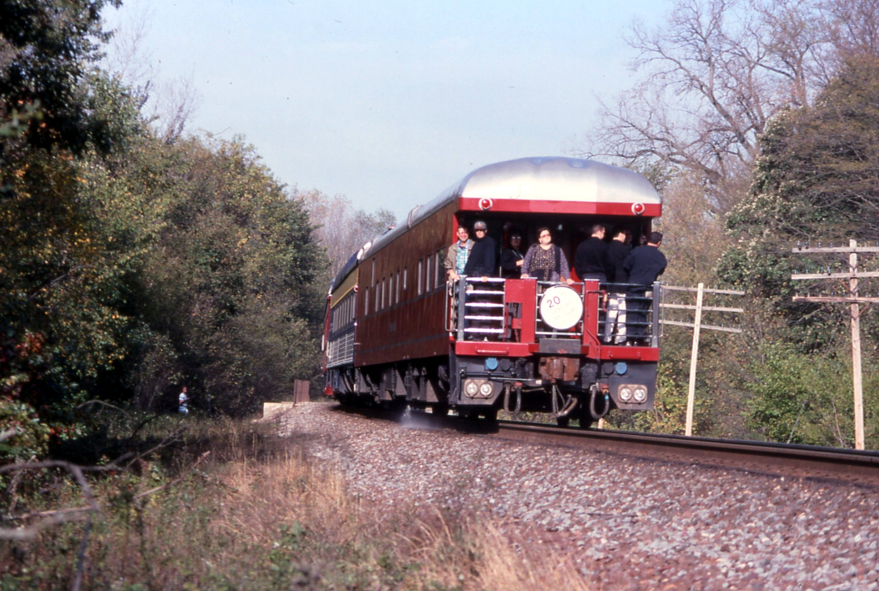 three people are riding on the side of a train going down the track