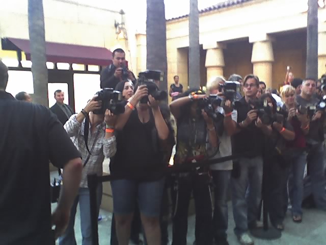a crowd of people stand around two men with cameras