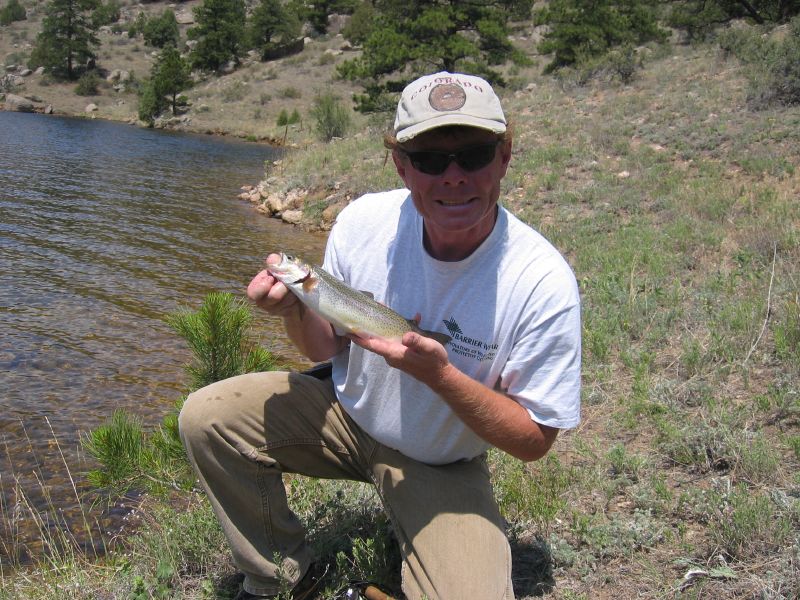 a man crouching down next to a body of water holding a fish