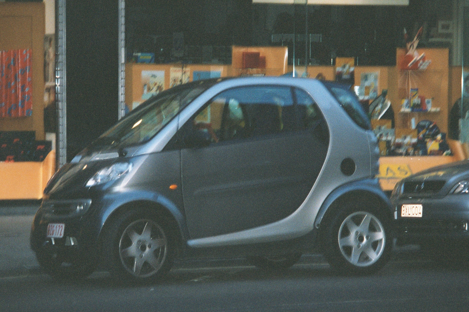 a gray and black small car and cars on a street