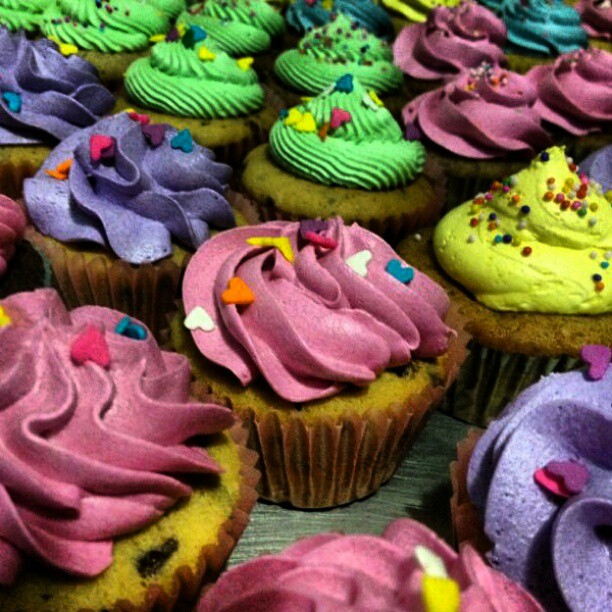 a display of various colored cupcakes with sprinkles