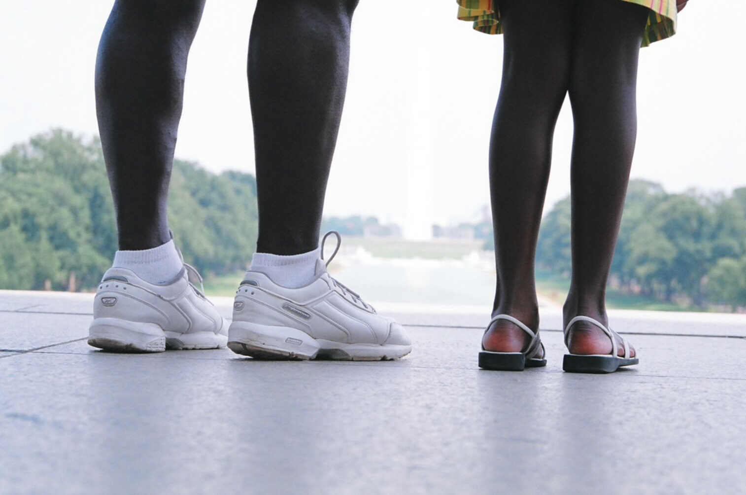 two people in white shoes stand in front of trees