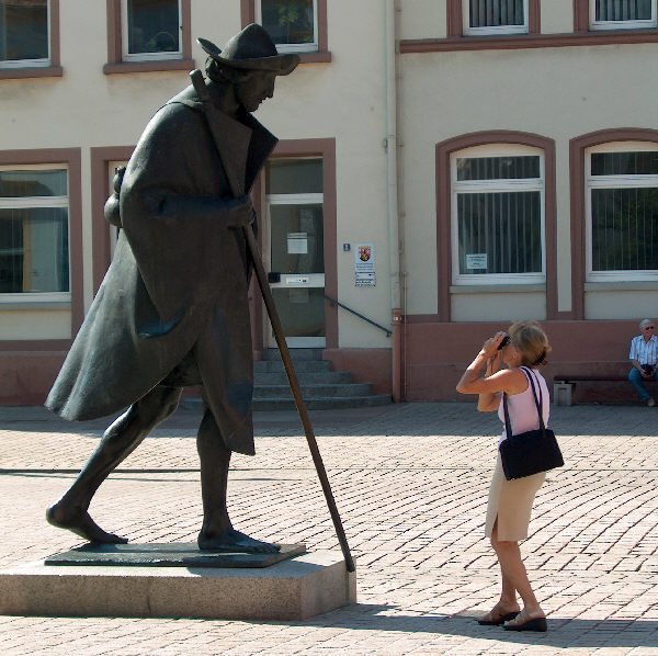 a woman taking a po of a statue of a man with a cane