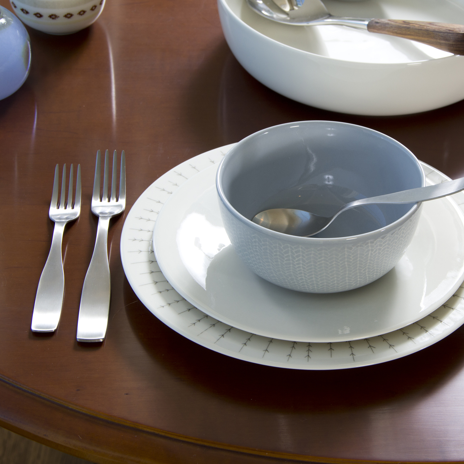 an empty white bowl on a wooden table with silverware