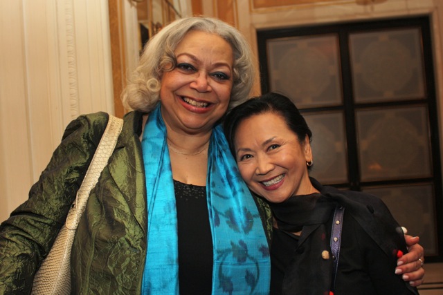 two women smile together at a party in a room