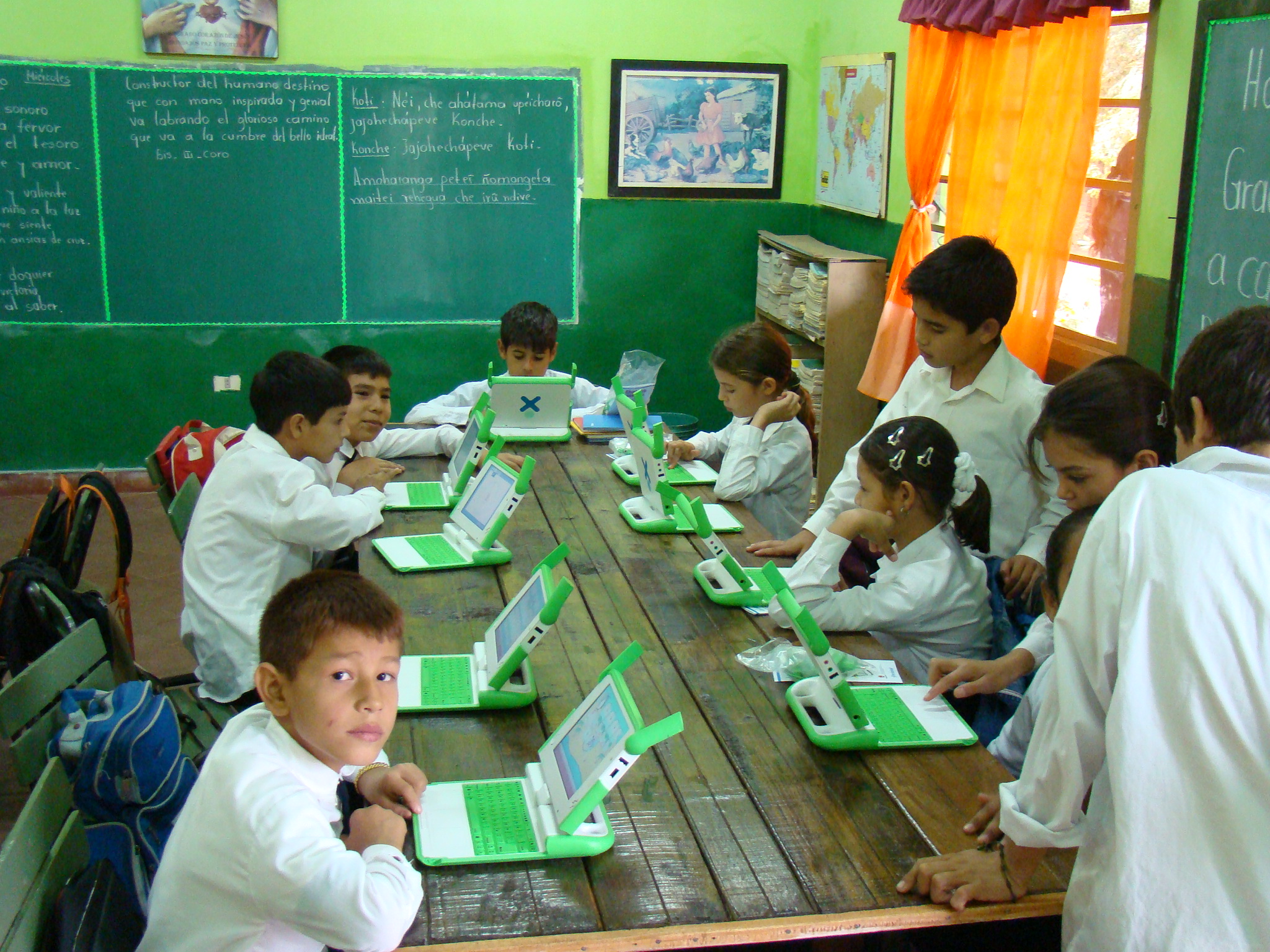 several children sitting at a wooden table in front of laptops