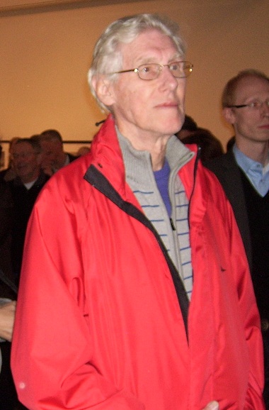 an elderly woman wearing a red jacket and glasses in a crowd