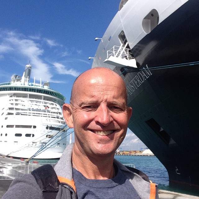 man standing on dock with large cruise ship in background