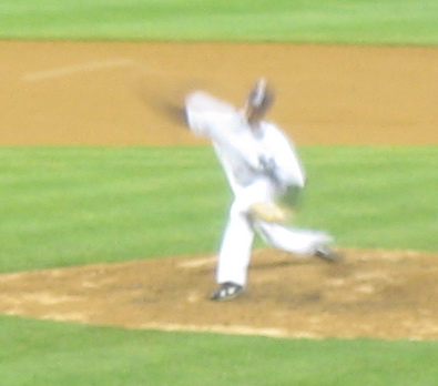 a man wearing white throwing a baseball on a field