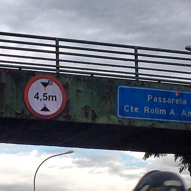 there is a metal sign on the bridge above a vehicle