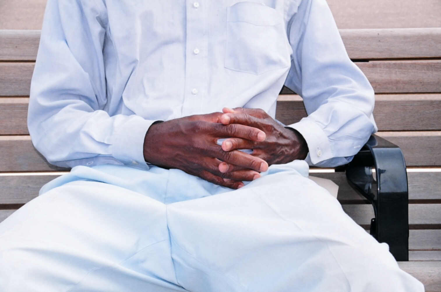 an african man with his hands together sitting on a park bench