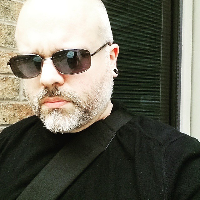 bald man with thick hair wearing sunglasses, looking off camera