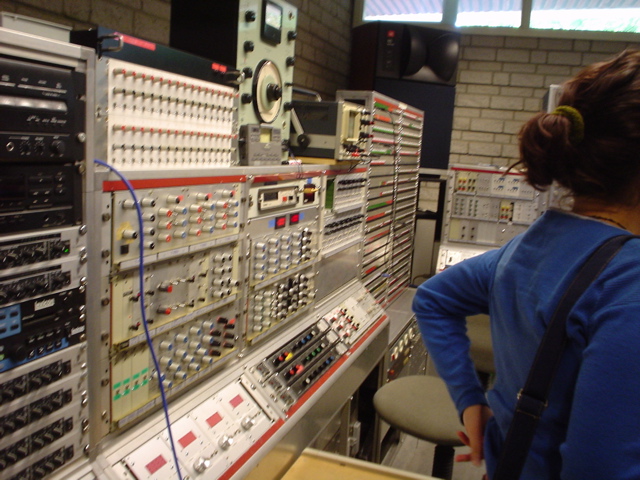 a large row of electrical panel with a woman in a blue top and a man with a black jacket looks at a wall full of electronic equipment