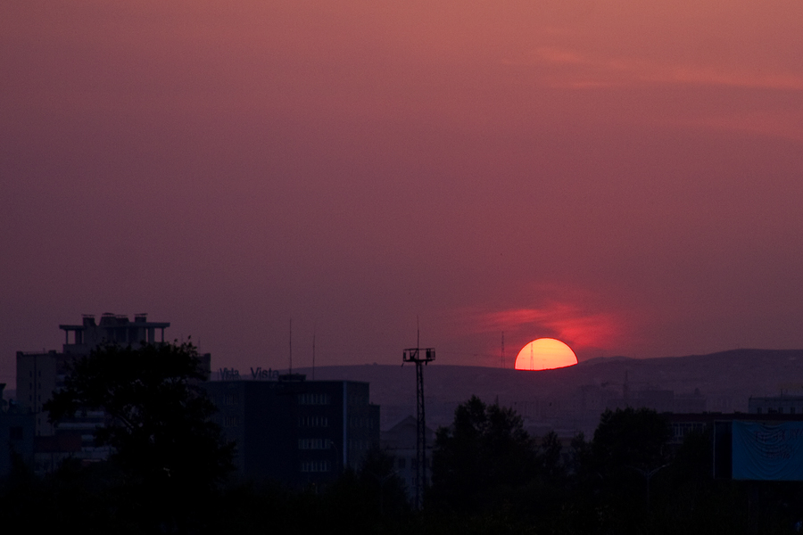 the sun setting on a hazy evening with buildings in the background