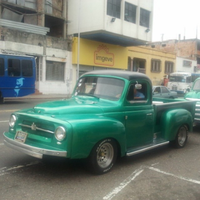 an old green truck driving down the street
