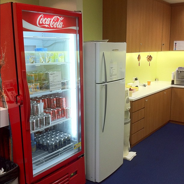 a coke machine and refrigerator next to each other in the kitchen