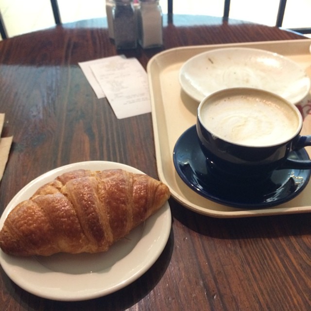 there is a croissant, a cup of cappuccino, and a plate on the table