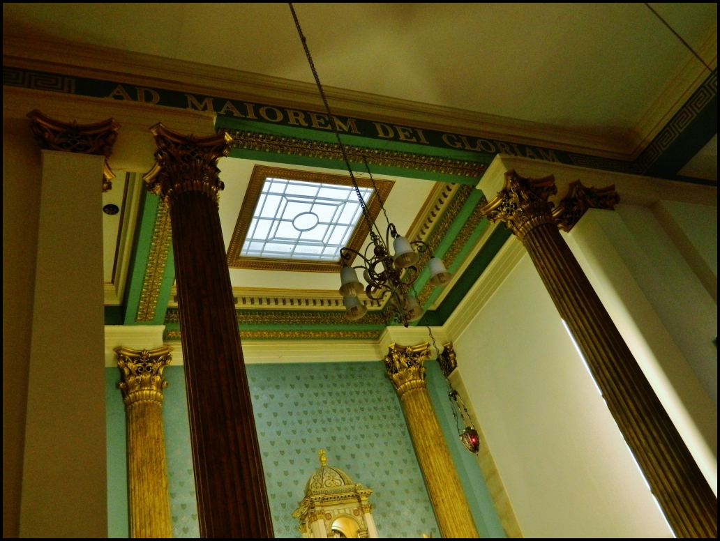 a clock sitting above a golden column and window in a room