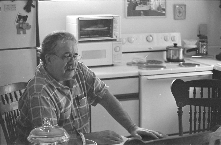 a man sitting at a table with glasses on his head and looking into the kitchen
