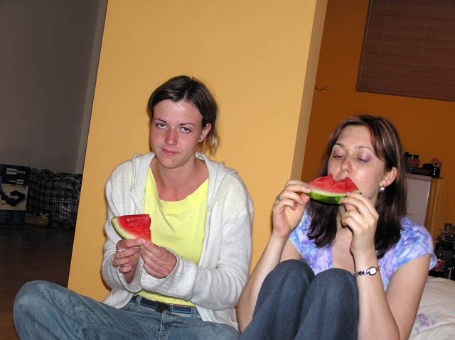 two women sitting on the floor while eating a slice of watermelon