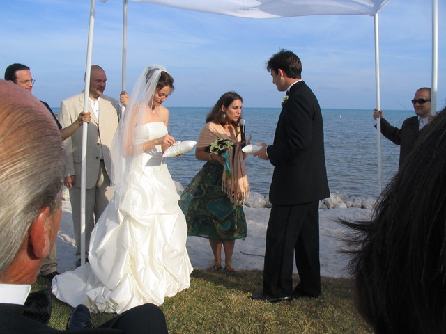 a bride and groom stand under an umbrella beside the ocean