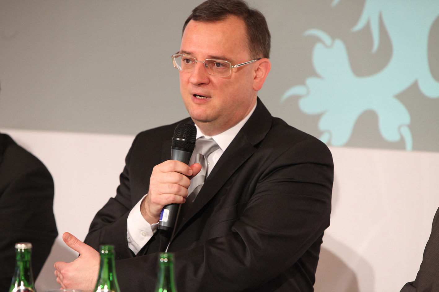 a man in a suit holds a microphone to speak into the crowd