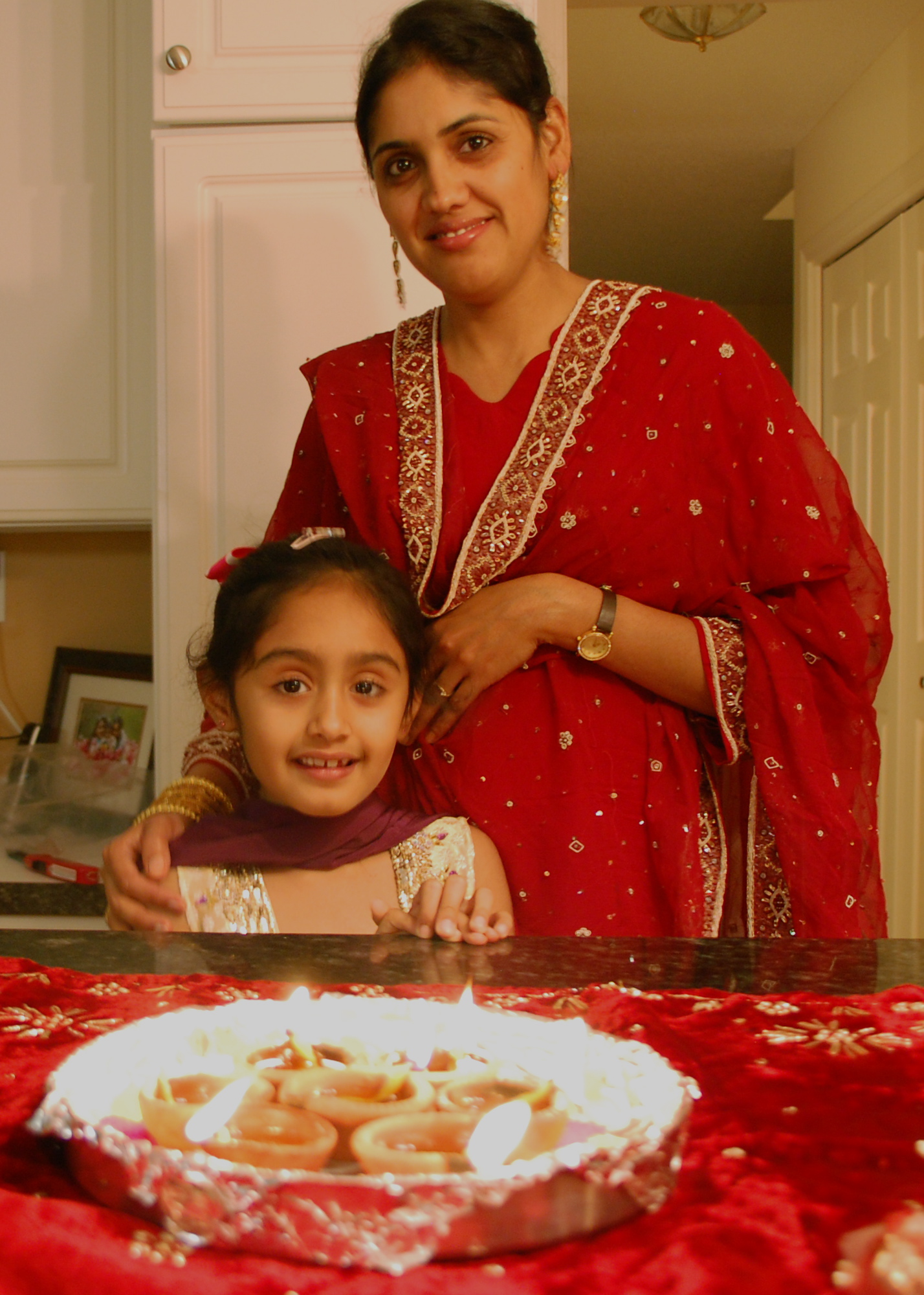 an indian woman smiles at the camera as she stands in front of a plate with small cakes on it