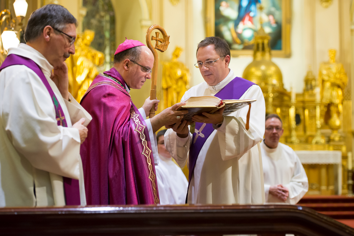 priests wearing red, white, and blue robes look at a book