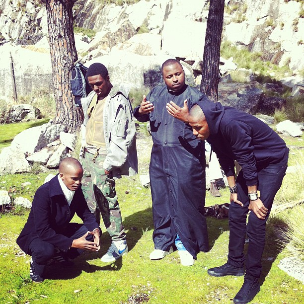 several people in black suits standing around while one person uses his cell phone