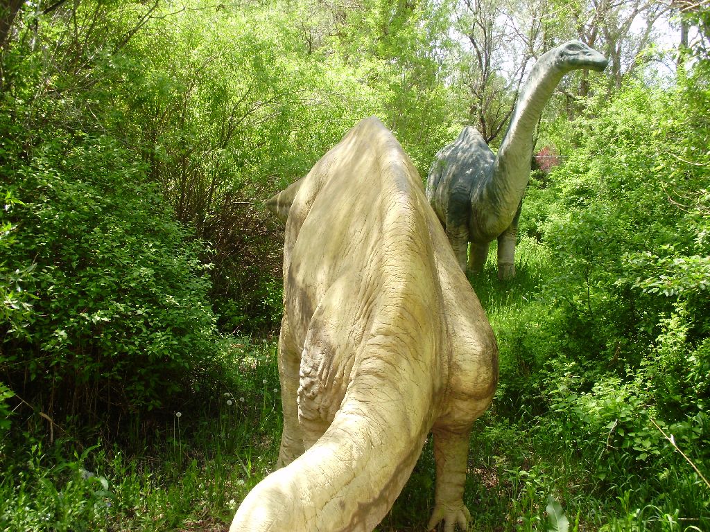 a large statue of a dino is near a bush