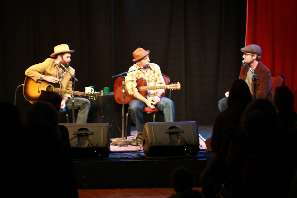 two men sitting on stage playing guitar and singing