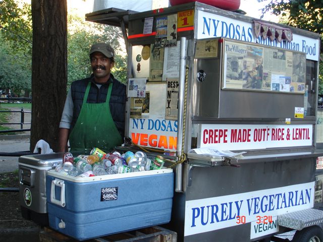 a vendor behind a vendor cart selling produce