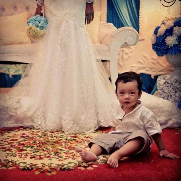a small boy sitting on the floor next to a wedding dress
