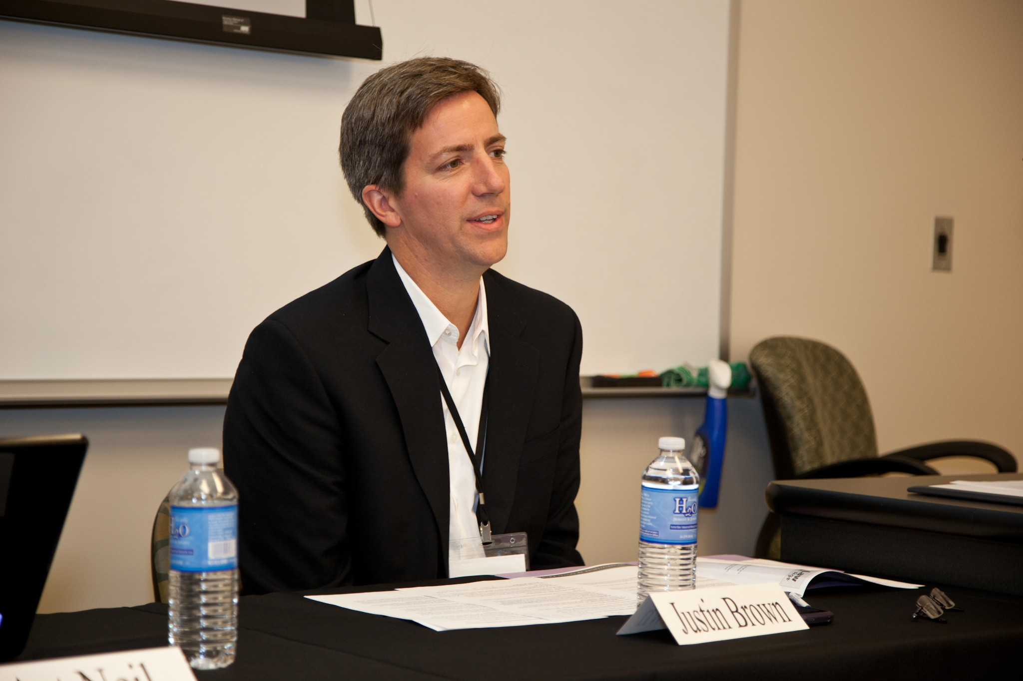 a man sits at a table with bottled water and talks into his microphone