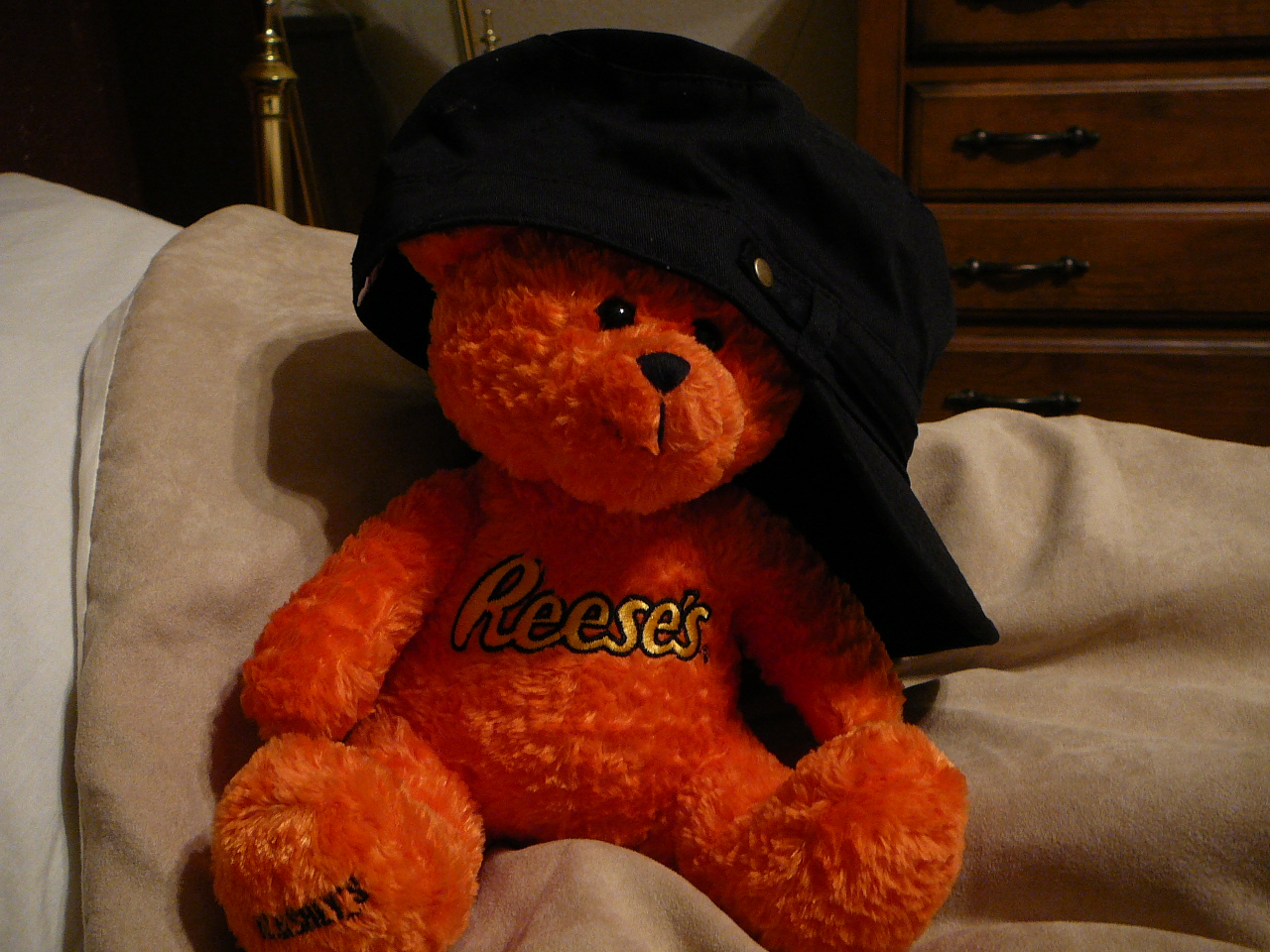 a red teddy bear with a black hat sits on top of a bed