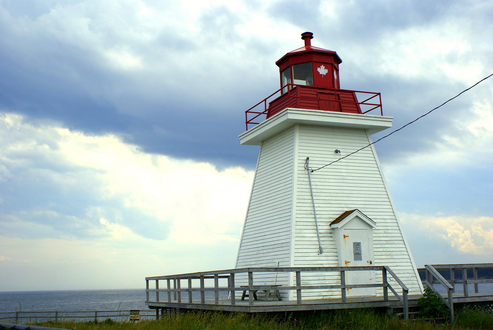 the light house is next to the sea under a gray cloudy sky