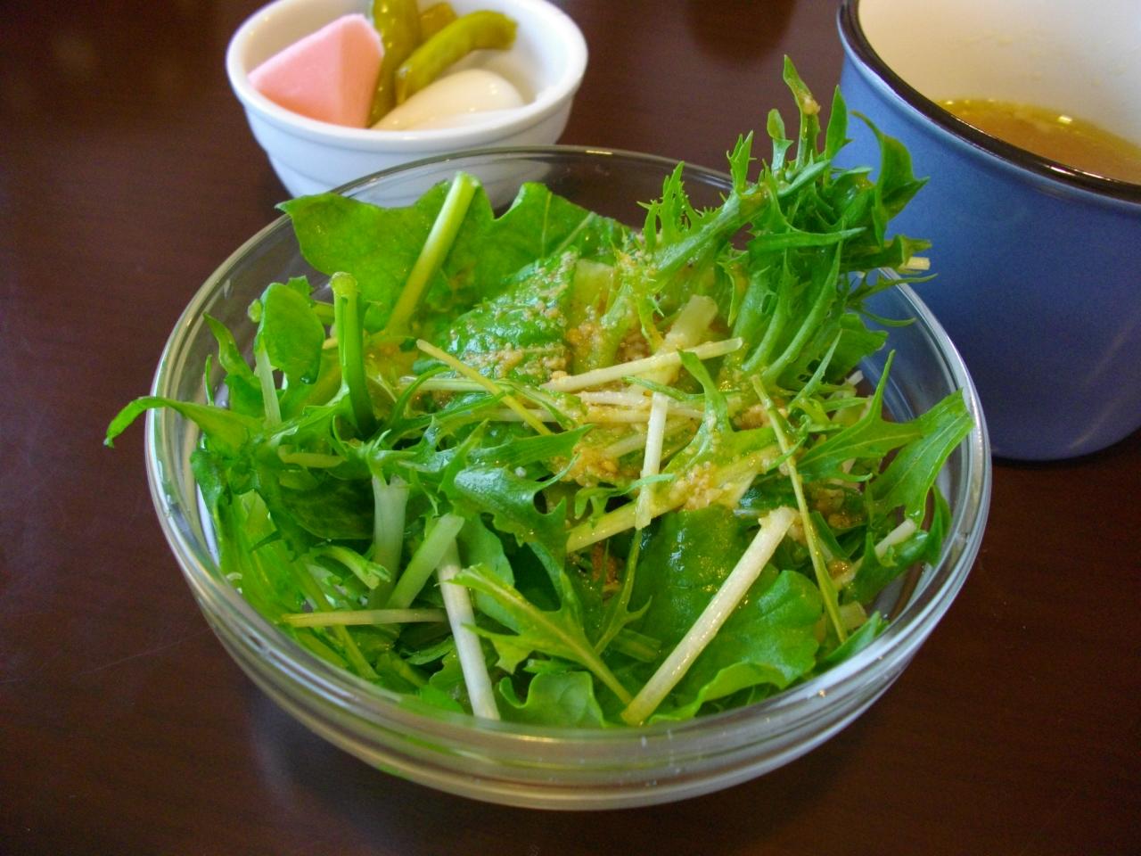 a salad on a wooden table with a small container of pickles