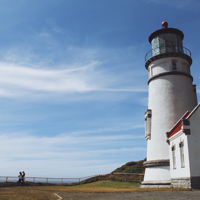 two people walking on a paved pathway past a lighthouse